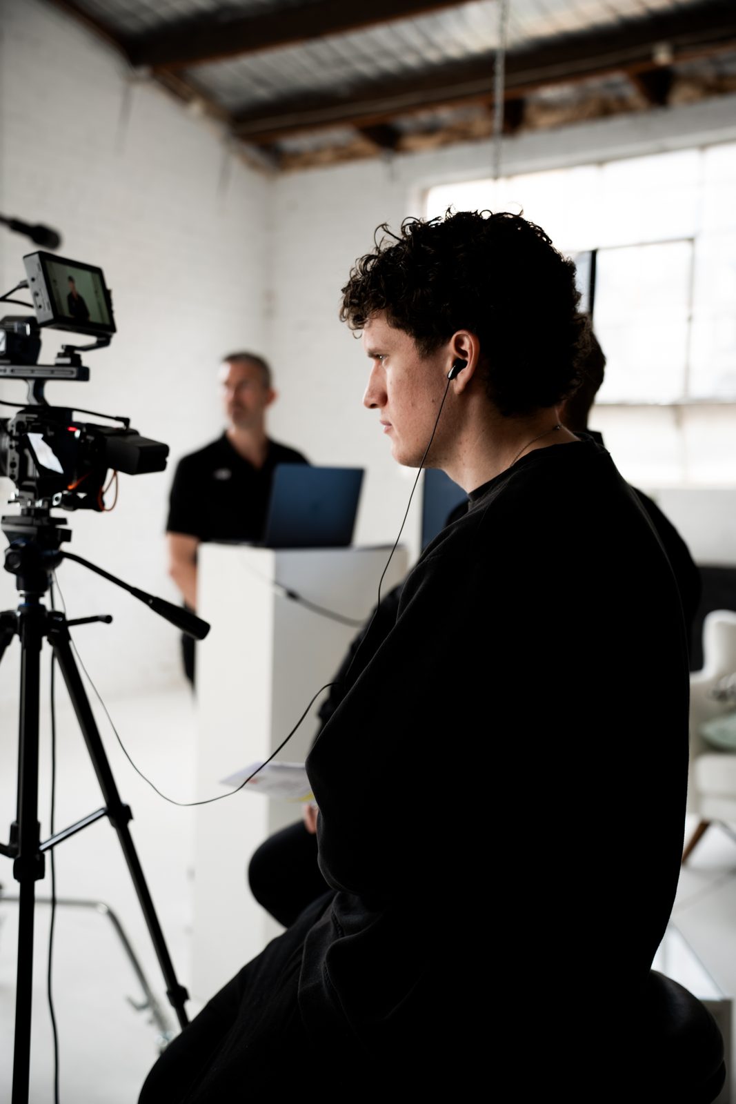 The crew at work on a studio set, camera on sticks and the monitor behind