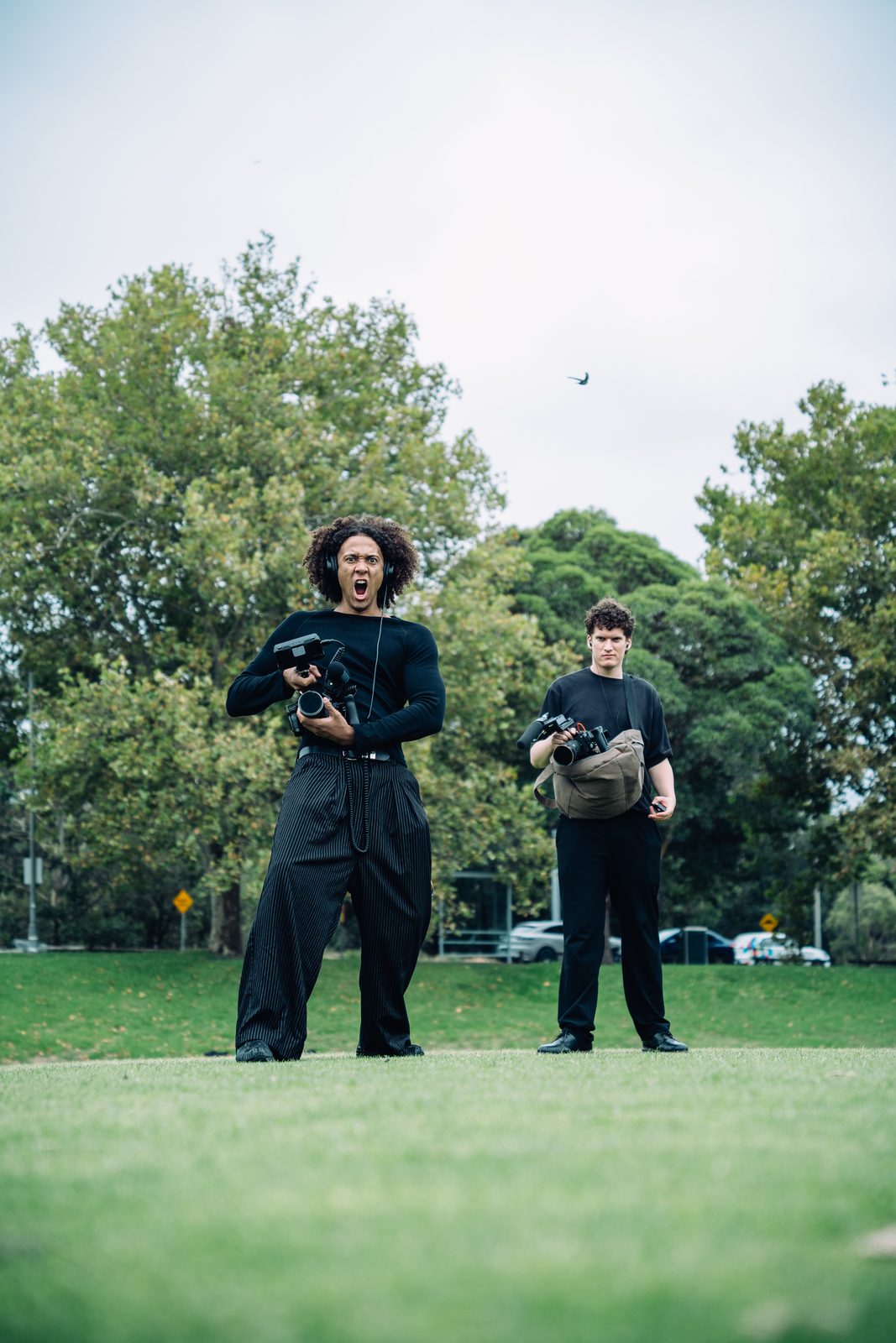 Two of the crew standing in a park with their cameras, one mid shout