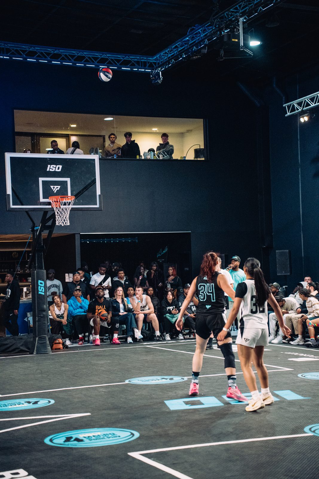A basketball game in play under court lights, filmed courtside