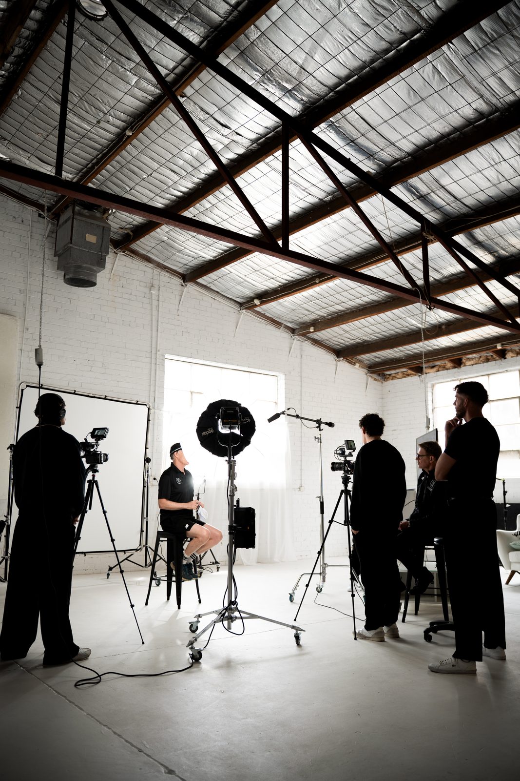 The full crew around a seated subject on a studio set, lights and cameras rigged